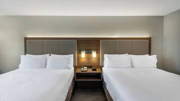 Een hotelkamer met twee bedden, een houten hoofdeinde, een nachtkastje met telefoon en een wandlamp.