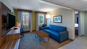 A modern hotel room with a flat-screen TV, a wooden desk, a blue sofa, and a small coffee table. - Holiday Inn Express State College at Williamsburg Square by IHG (State College)
