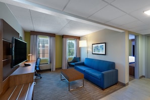 Habitació d'hotel moderna amb televisió de pantalla plana, escriptori de fusta, sofà blau i taula de cafè petita.