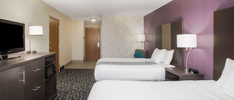 Une chambre d’hôtel avec deux lits, une télévision, un bureau et une salle de bain visible au fond.