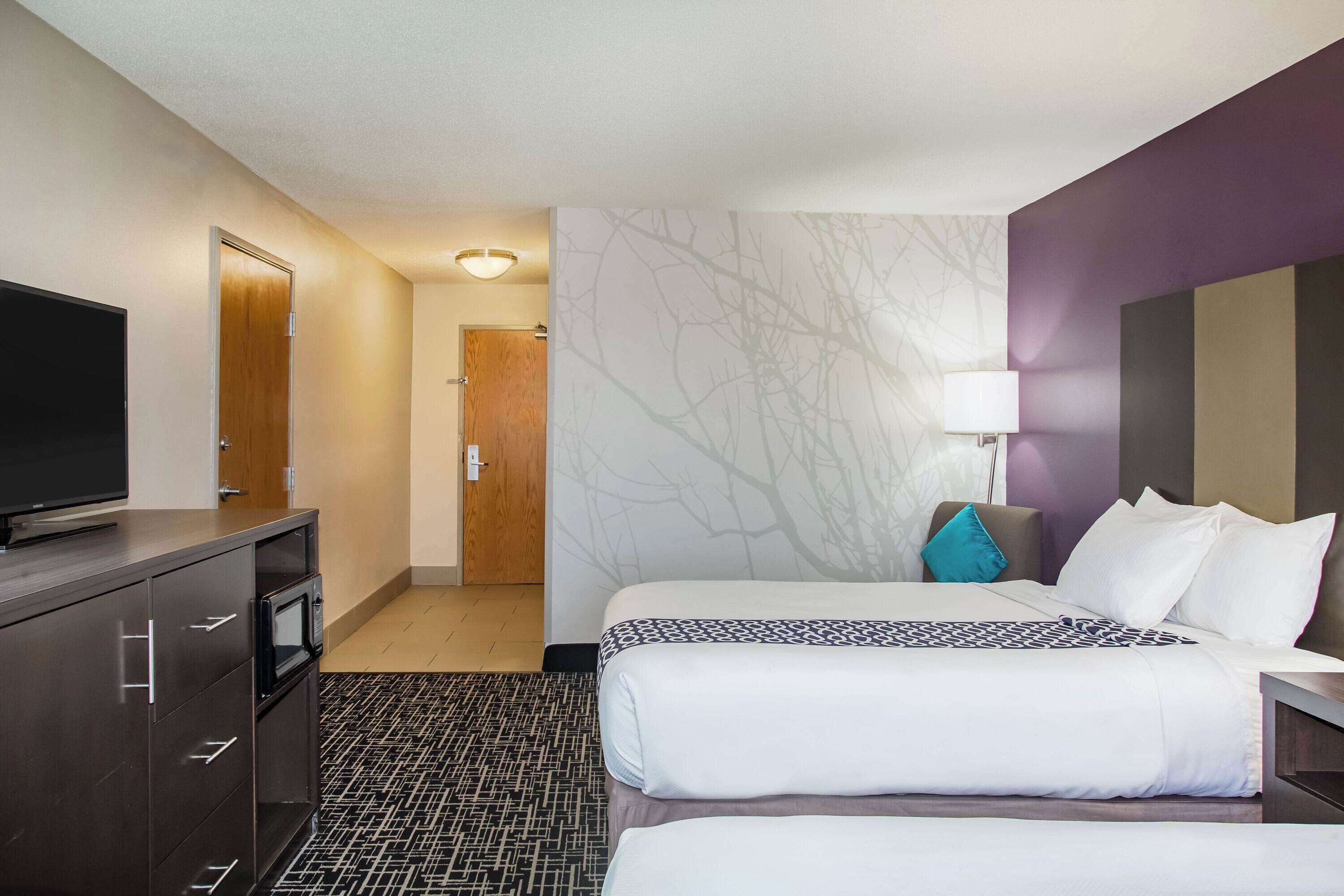 Une chambre d’hôtel avec deux lits, un téléviseur posé sur une commode, un tapis à motifs et un mur décoré d’un motif d’arbre.