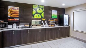 Mostrador de desayuno con microondas, cafeteras y una exhibición de frutas.
