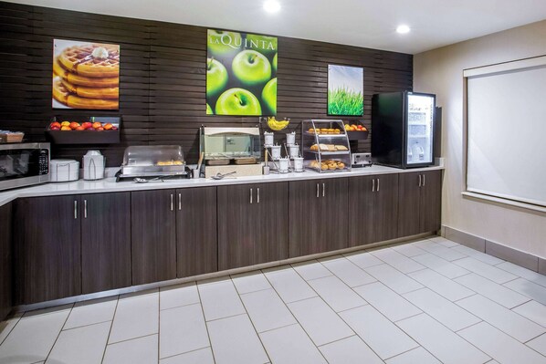 A breakfast bar with a microwave, coffee makers, and a fruit display.
