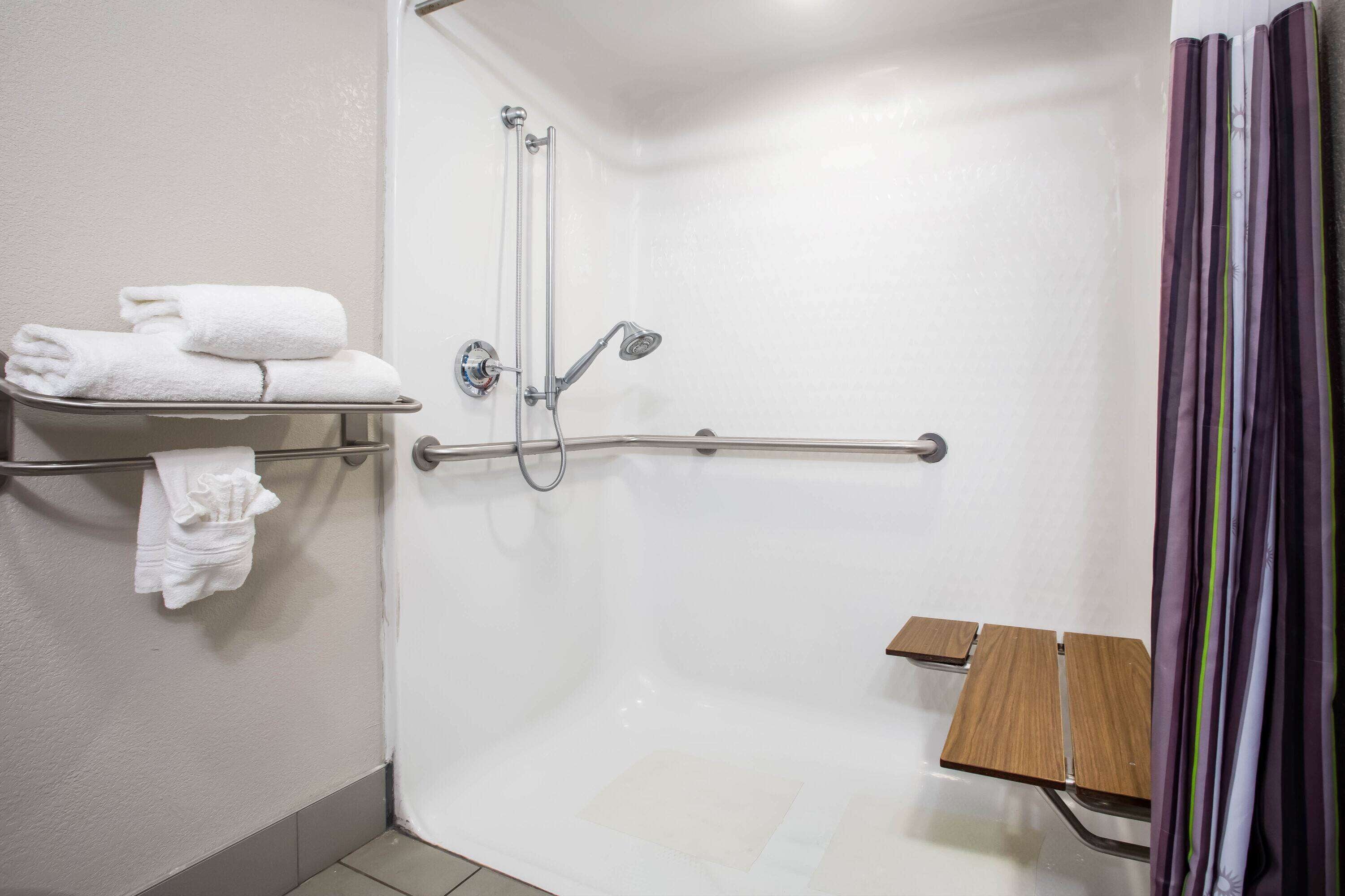 A shower area with a grab bar, a shelf with towels, and a wooden bench.