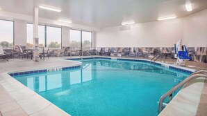 Una piscina con agua azul cristalina, rodeada de sillas de descanso y un muro de azulejos.