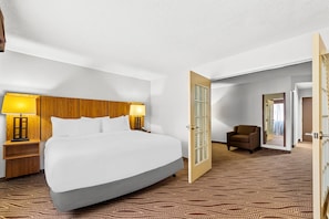 Ein Hotelzimmer mit einem großen Bett, zwei Nachttischlampen, einem Holzkopfstück, einem gemusterten Teppich und einer Tür zu einem anderen Raum.