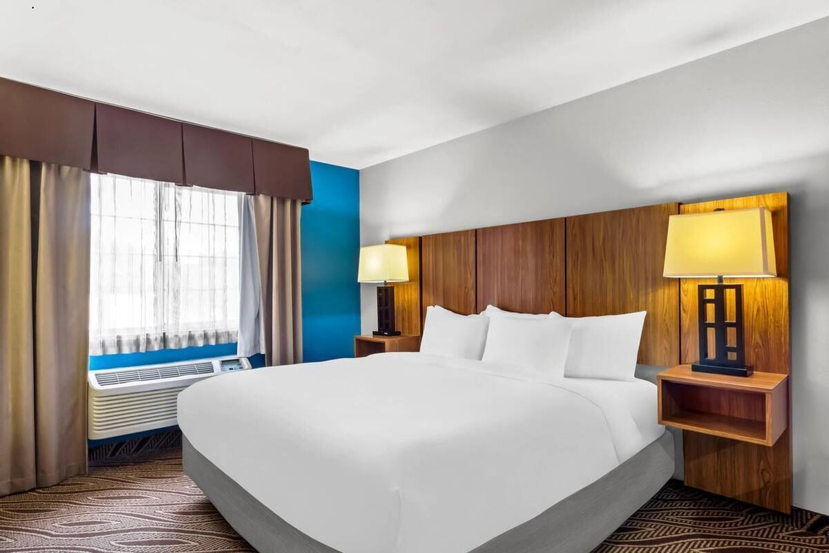 Une chambre d’hôtel avec un grand lit, deux lampes de chevet, une fenêtre avec des rideaux et un radiateur fixé au mur.