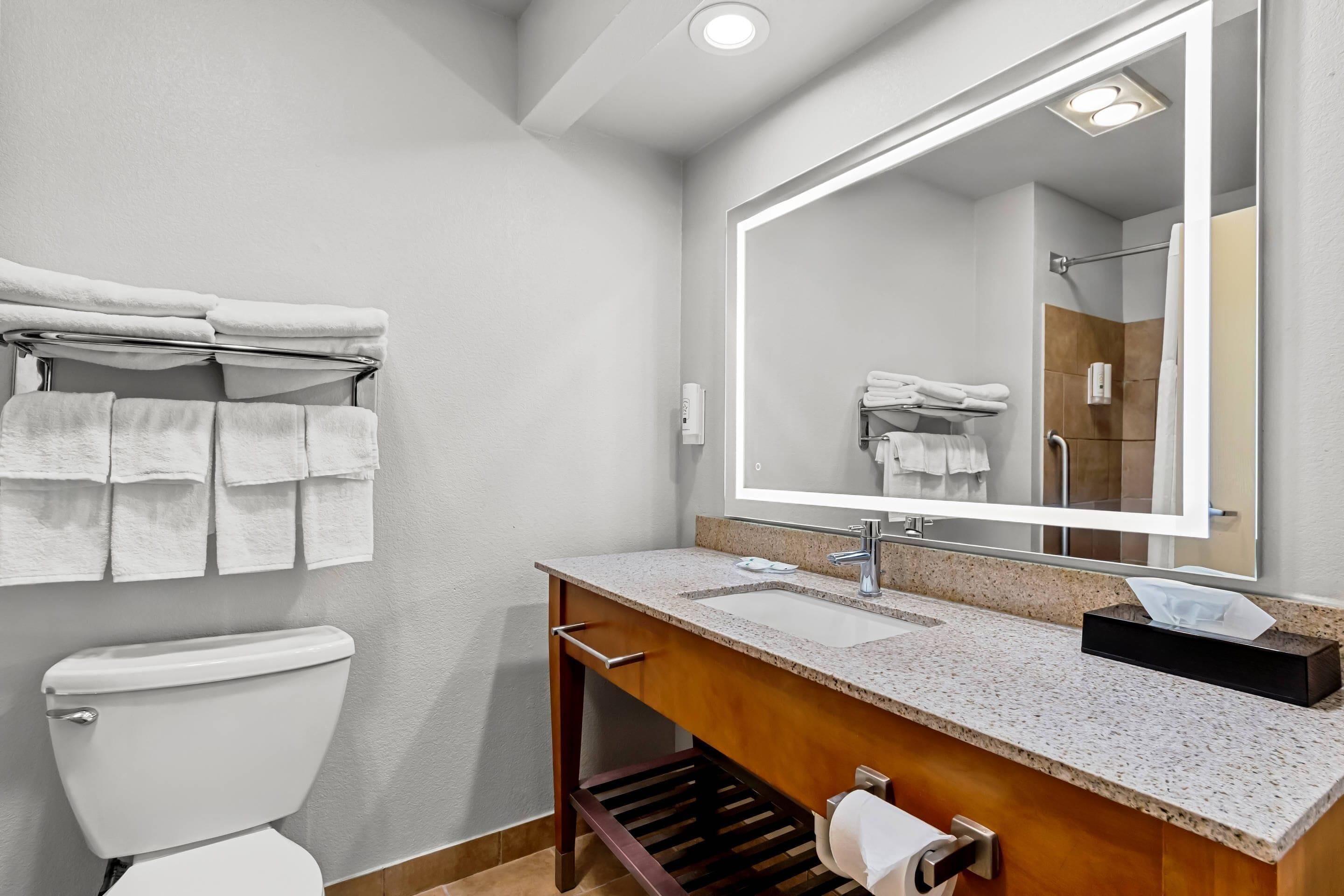A modern bathroom with a white toilet, a sink with a mirror above it, and a towel rack with multiple towels.