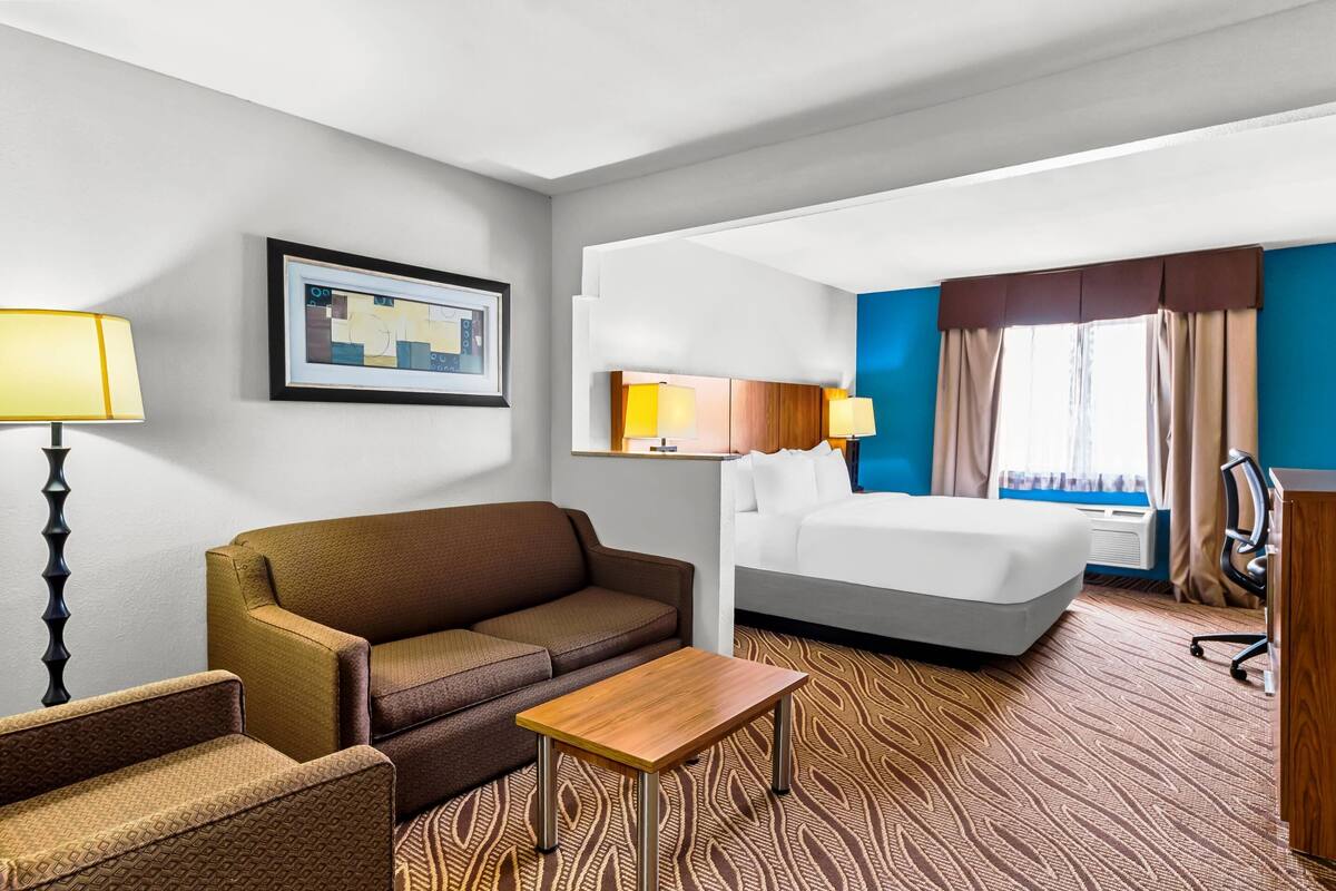 Une chambre d’hôtel comprenant un lit, un canapé, une petite table, un bureau, une chaise et une lampe.