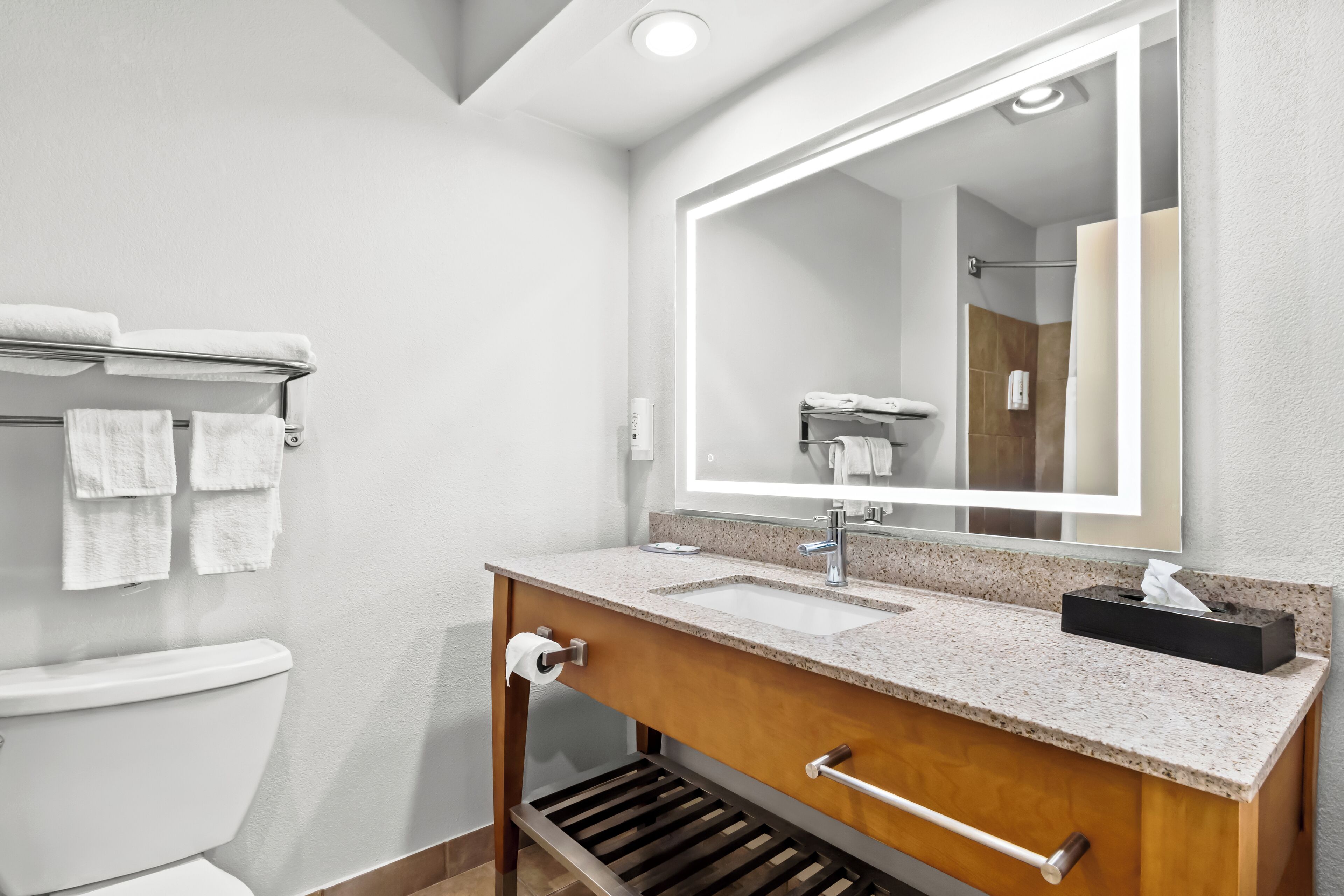 Un baño moderno con inodoro blanco, lavamanos con espejo y toallero con toallas blancas.