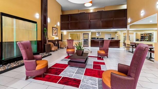 A lobby with a reception desk, seating area with armchairs, a potted plant, and a red and gray patterned rug. - Quality Inn & Suites San Antonio Airport - Stone Oak (San Antonio)
