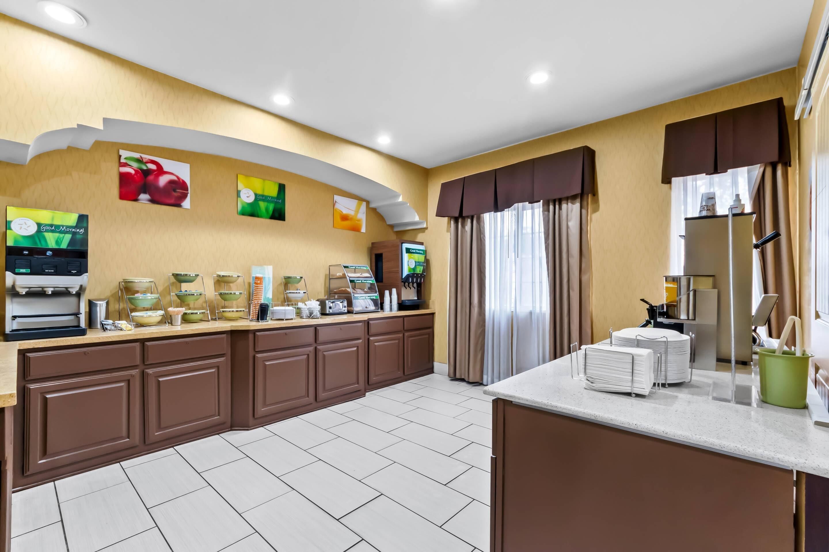 A hotel kitchen with a buffet setup, including a coffee station, a refrigerator, and a counter with stacked plates.