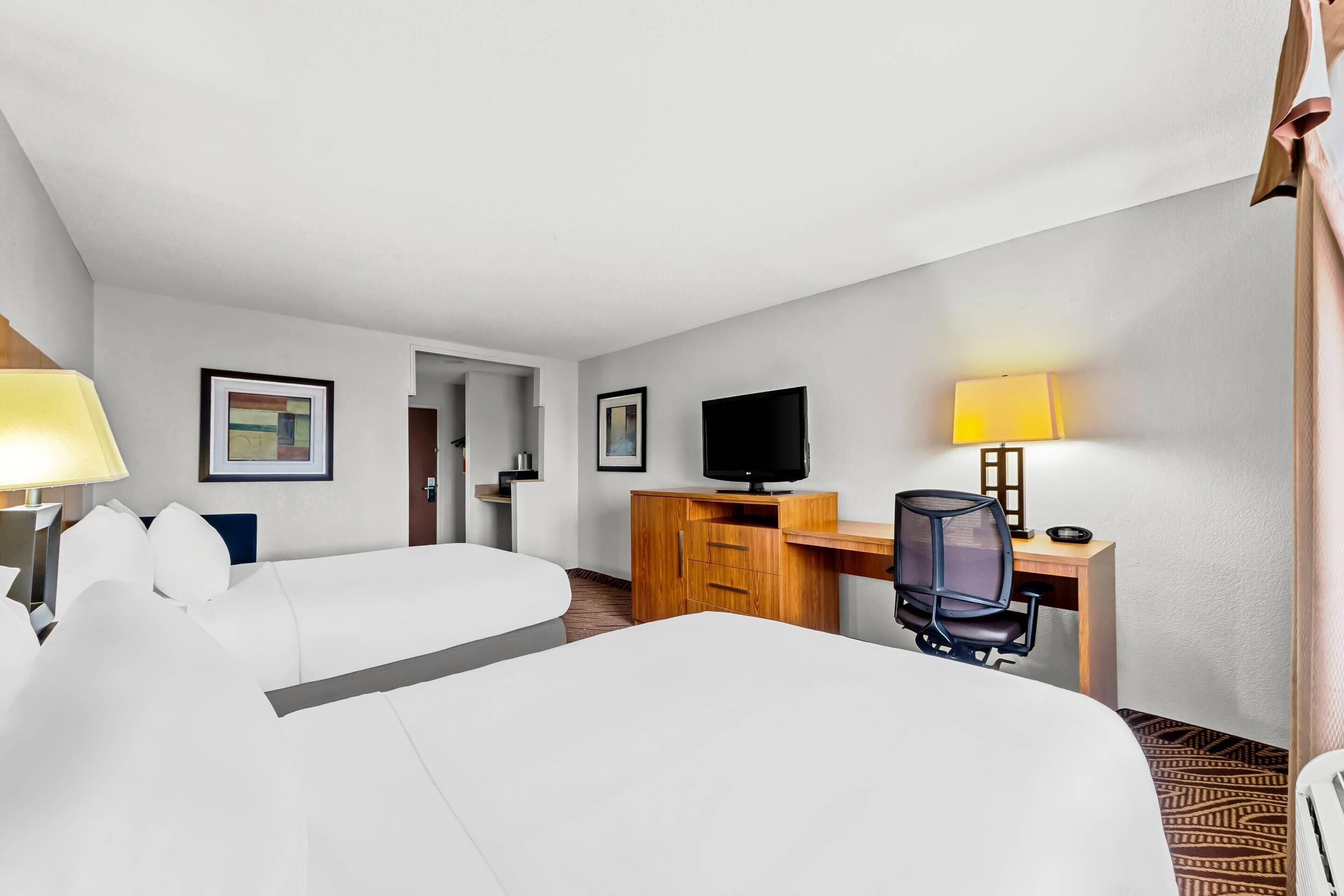 Ein Hotelzimmer mit zwei Betten, einem Schreibtisch mit Computer, einem Fernseher und einem Stuhl.