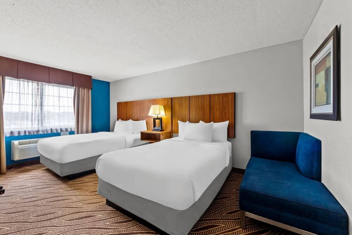 Une chambre d’hôtel avec deux lits, un canapé bleu, une lampe et un tableau encadré au mur.