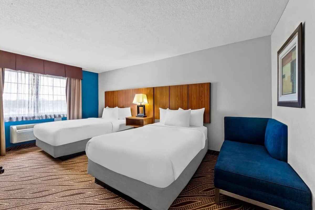 Quarto de hotel com duas camas, um sofá azul, uma luminária e um quadro na parede.