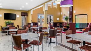 A modern dining area with multiple tables and chairs, a flat-screen TV mounted on the wall, and a large window providing natural light. - Quality Inn & Suites San Antonio Airport - Stone Oak (San Antonio)