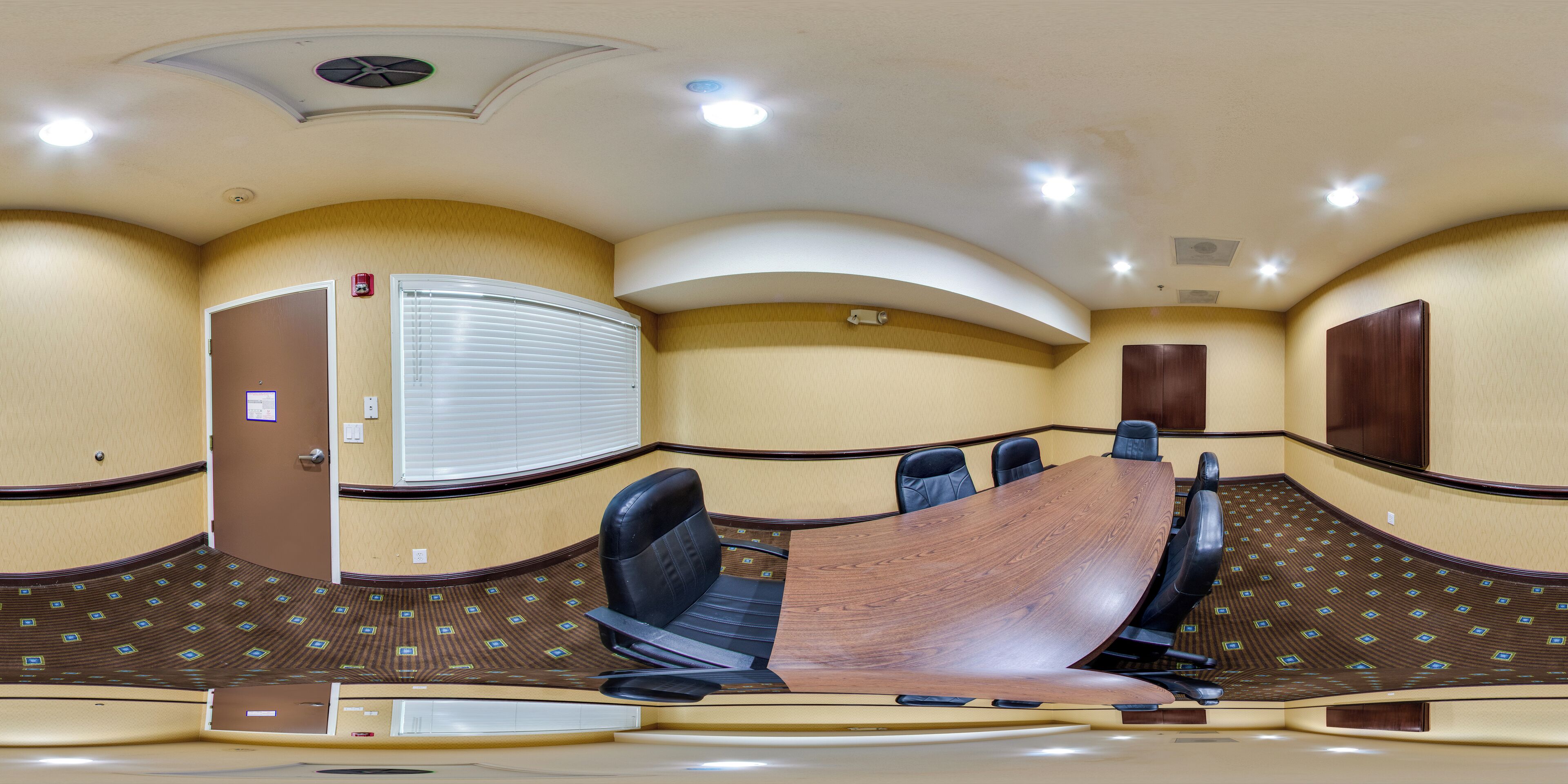 Un salón de conferencias con una mesa de madera curvada, sillas negras y paredes color beige.