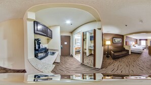 A panoramic view of a hotel room with a kitchenette, a sitting area with a sofa and armchairs, and a bedroom with a bed and a nightstand. - Quality Inn & Suites San Antonio Airport - Stone Oak (San Antonio)