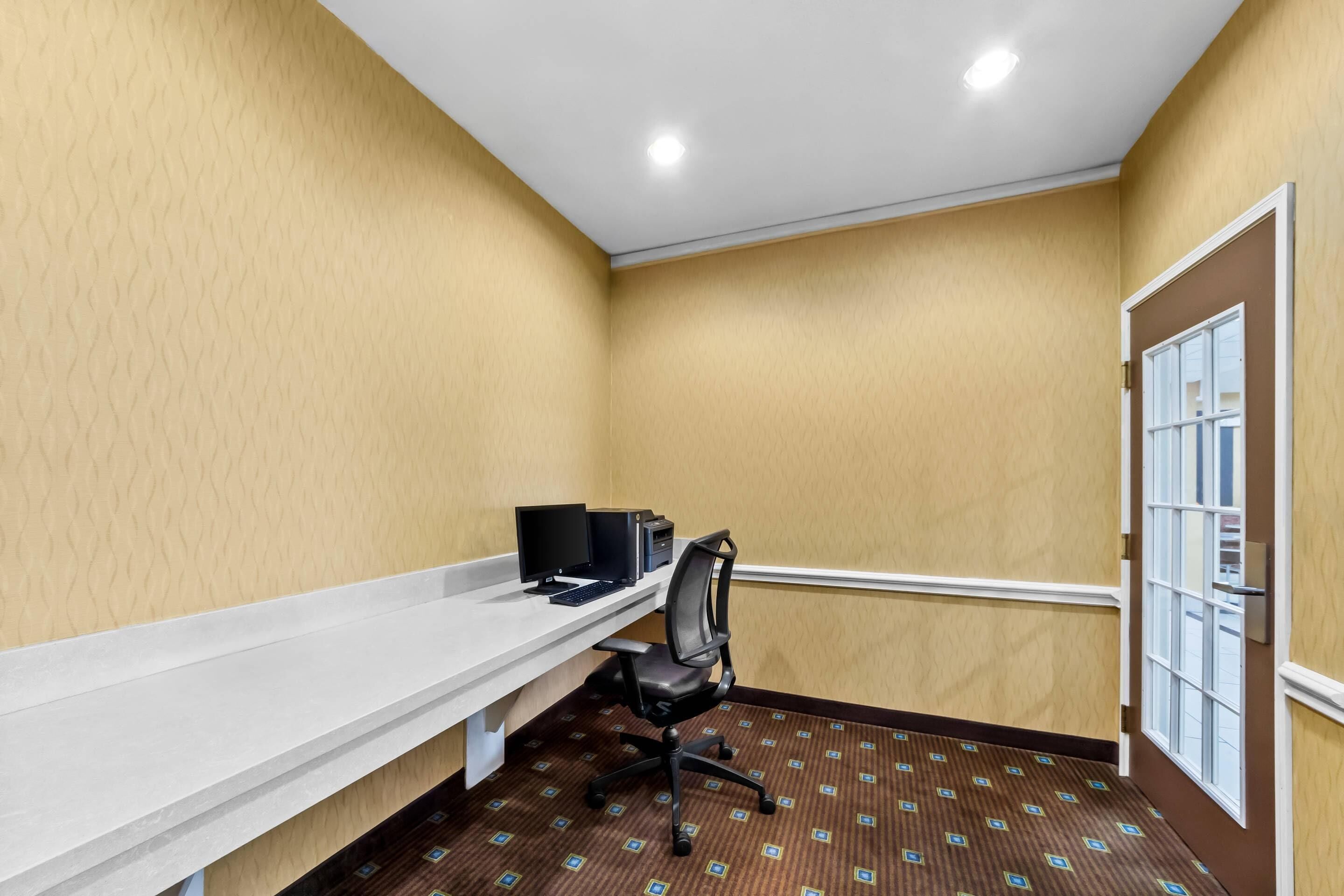 A hotel room with a white desk, black office chair, and a computer setup.