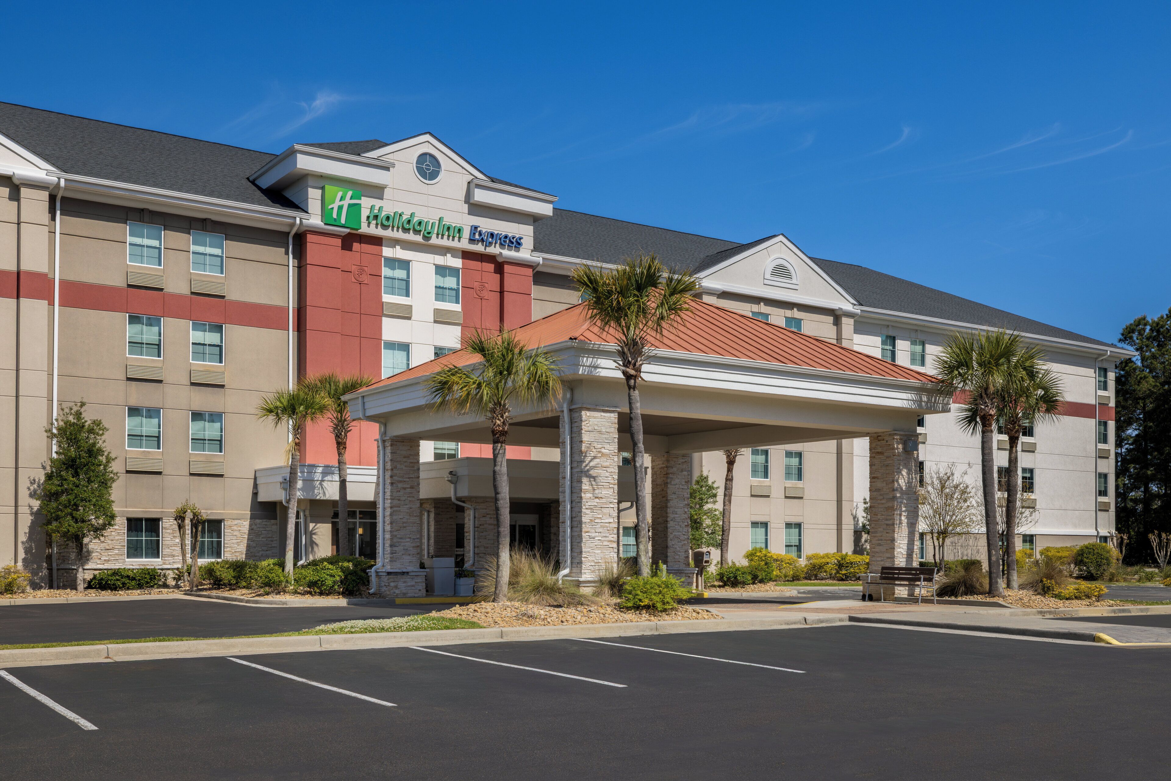 A hotel with a covered entrance, palm trees, and a parking lot.