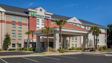 A hotel with a covered entrance, palm trees, and a parking lot.