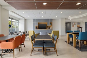 Un espace repas moderne avec une table centrale, des chaises disposées autour et un téléviseur à écran plat fixé au mur.
