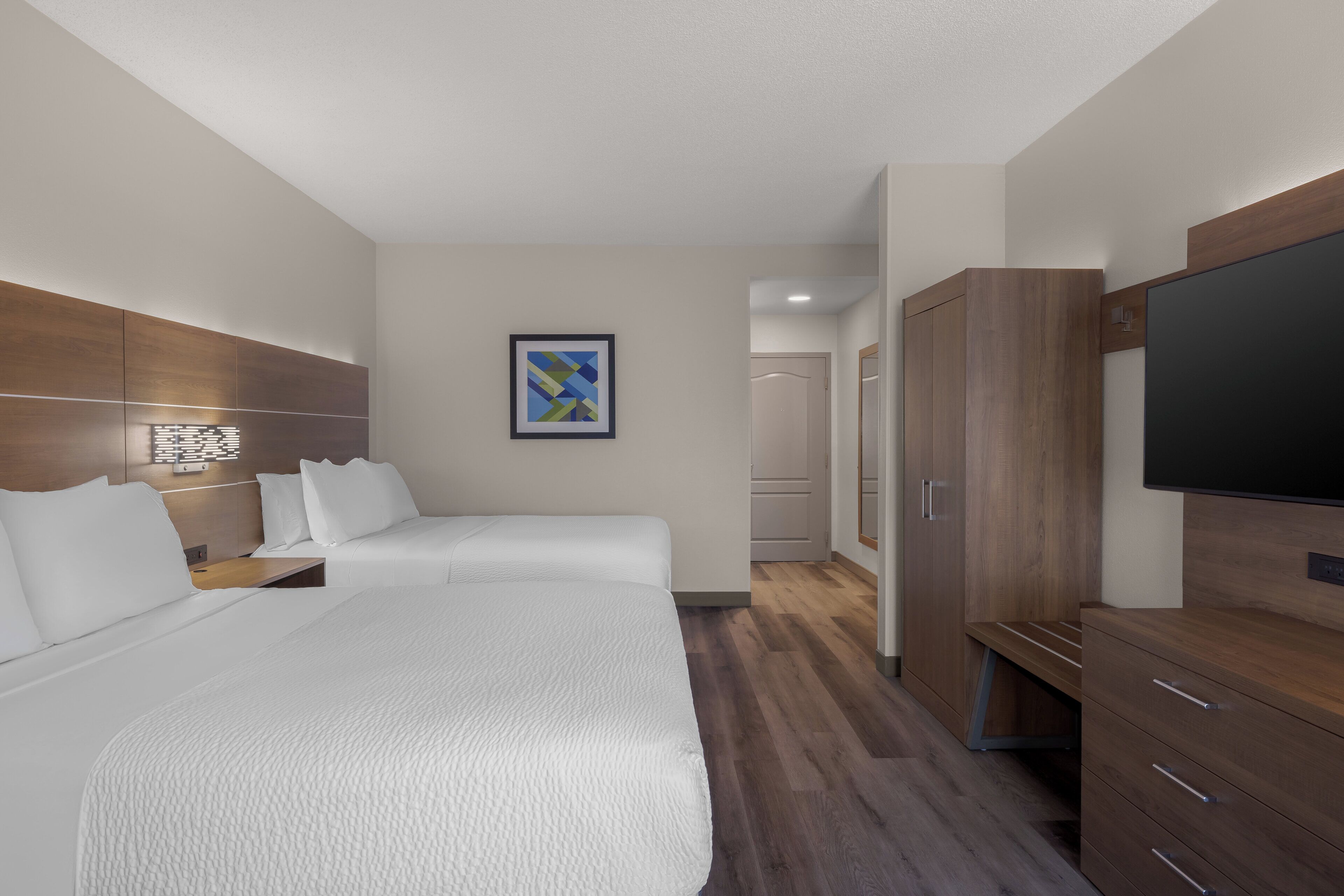 A hotel room with two beds, a TV, wooden wardrobe, and a painting on the wall.