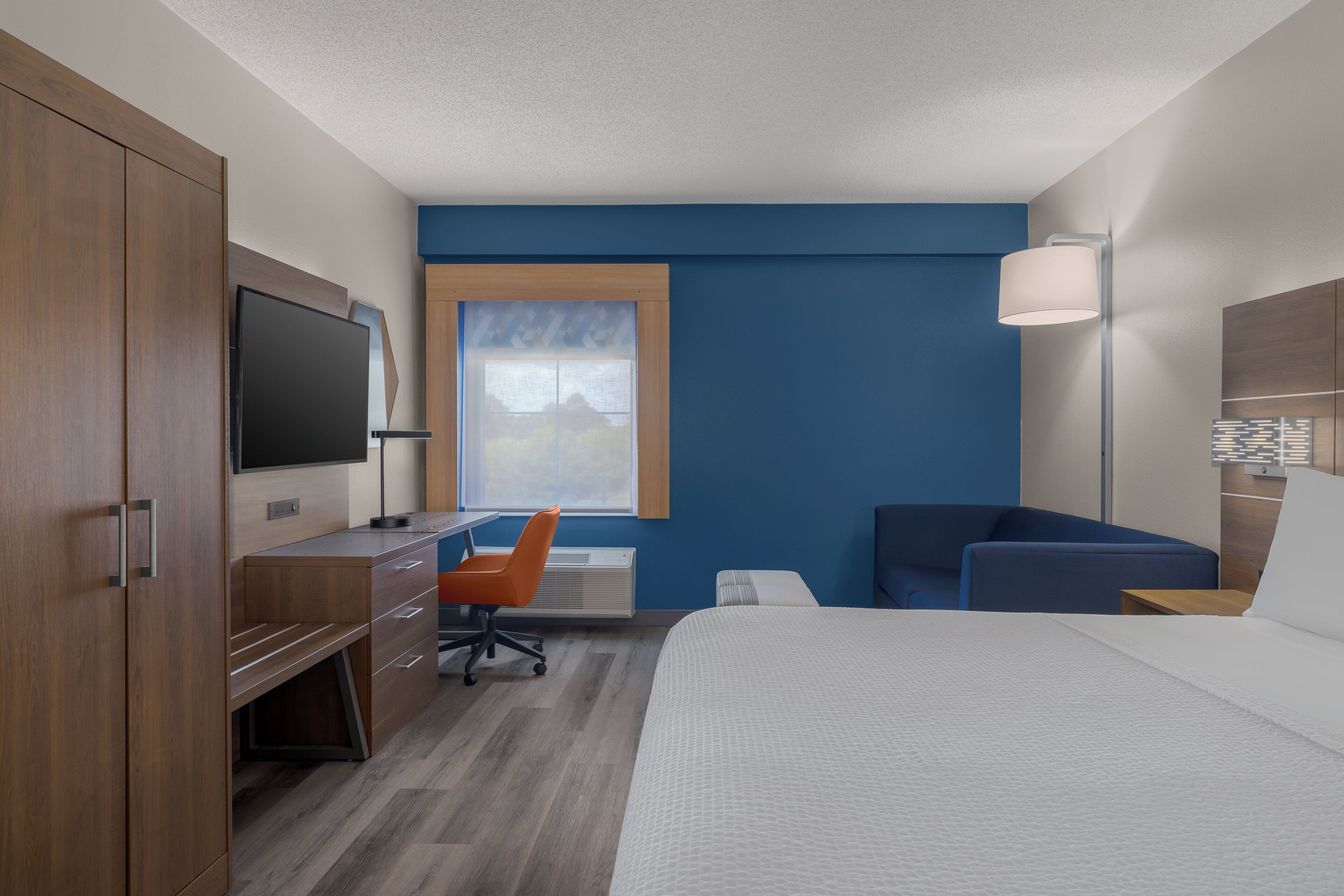 A hotel room with a bed, desk, chair, TV, and a window.