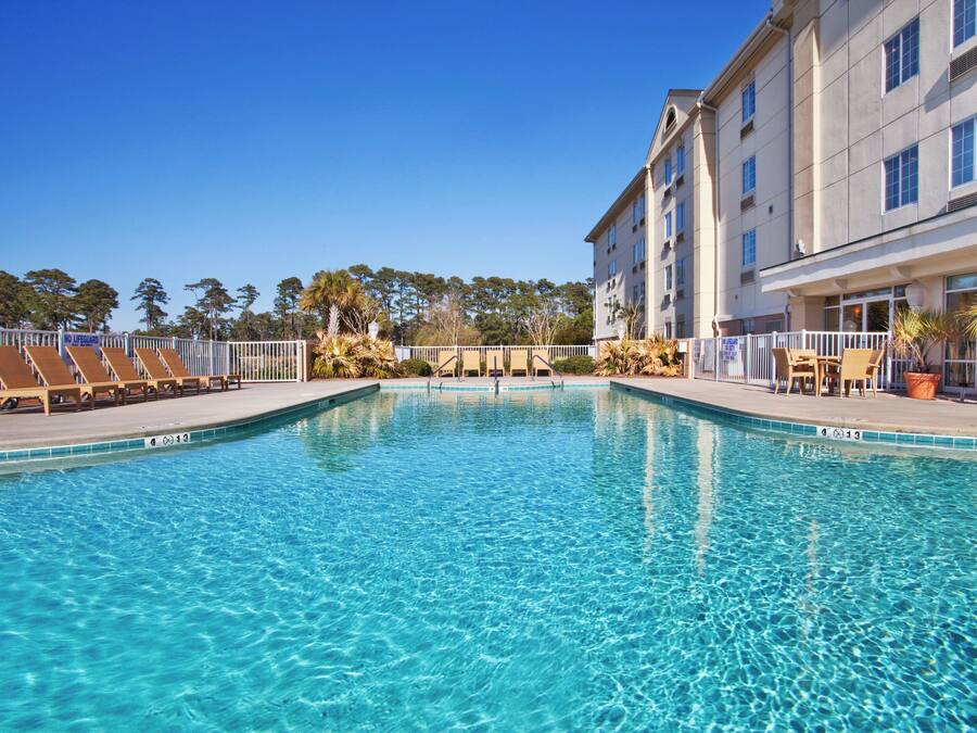 A clear swimming pool with lounge chairs and a building in the background.