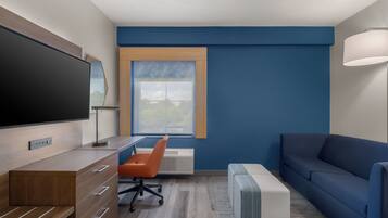 A modern room with a TV, wooden desk, orange chair, blue sofa, and a window with a view.