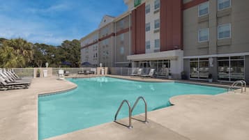 A hotel with a swimming pool, lounge chairs, and a clear blue sky.