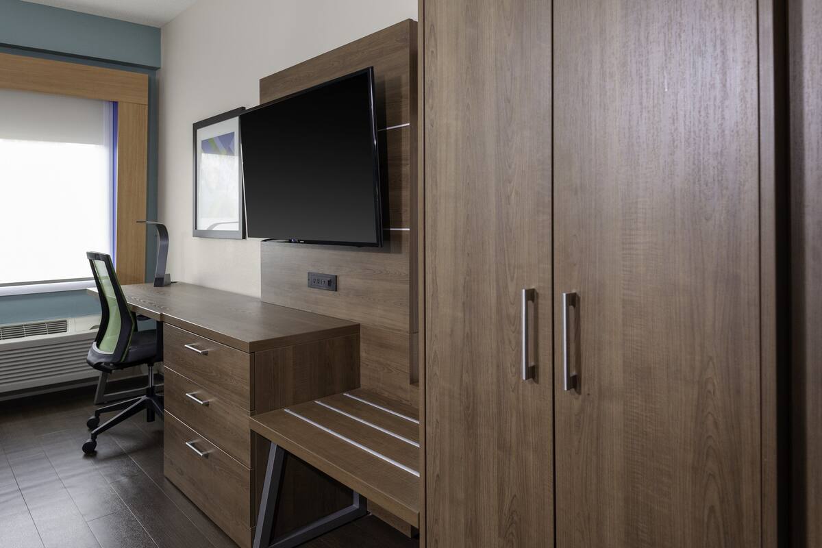 A modern office space with a wooden desk, a chair, a flat-screen TV mounted on the wall, and a large cabinet with drawers.
