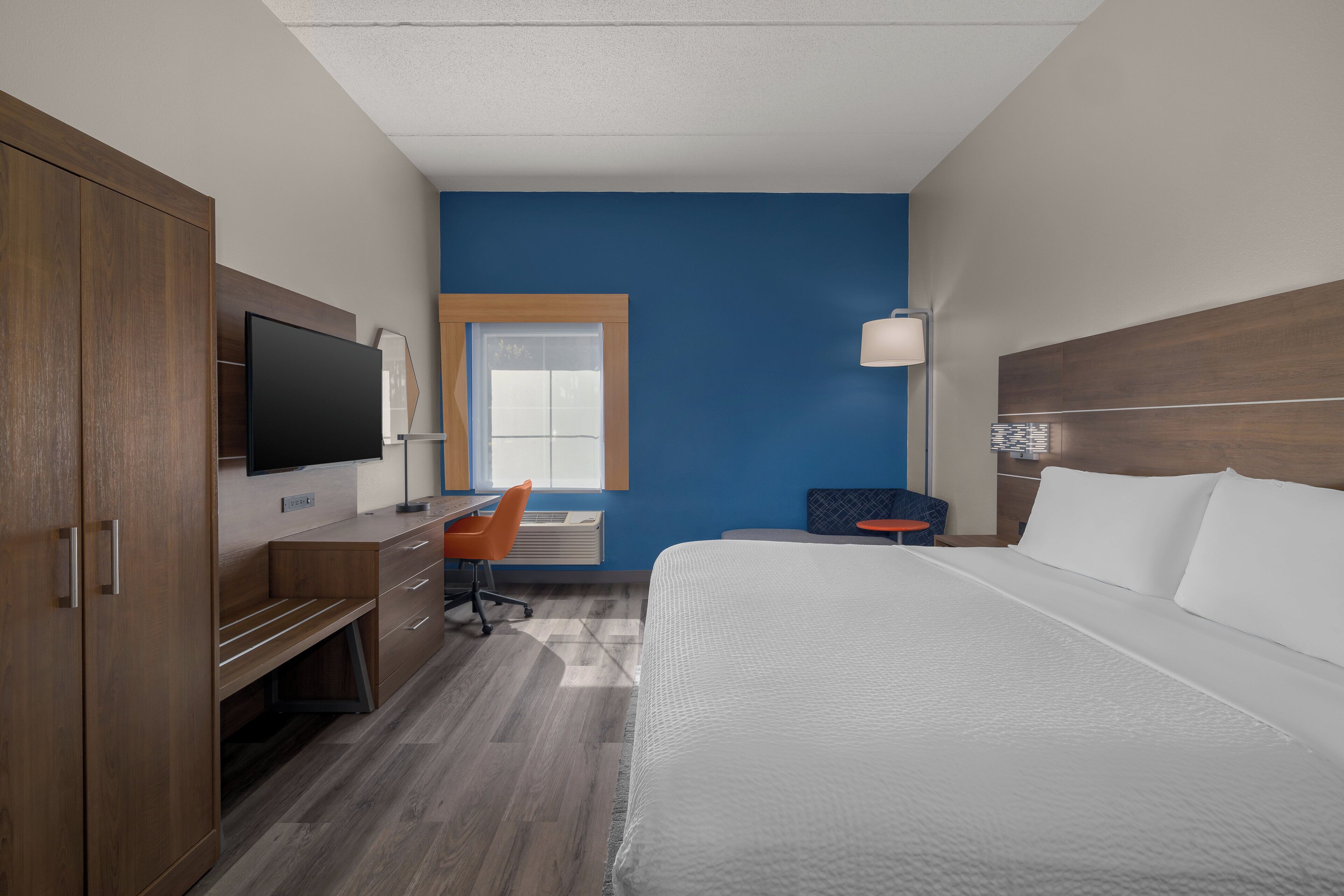 Quarto de hotel com uma cama, uma escrivaninha com cadeira, televisão e janela.