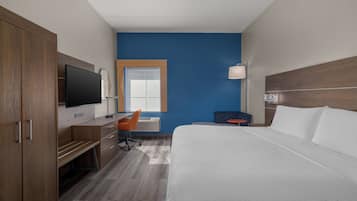 Quarto de hotel com uma cama, uma escrivaninha com cadeira, televisão e janela.