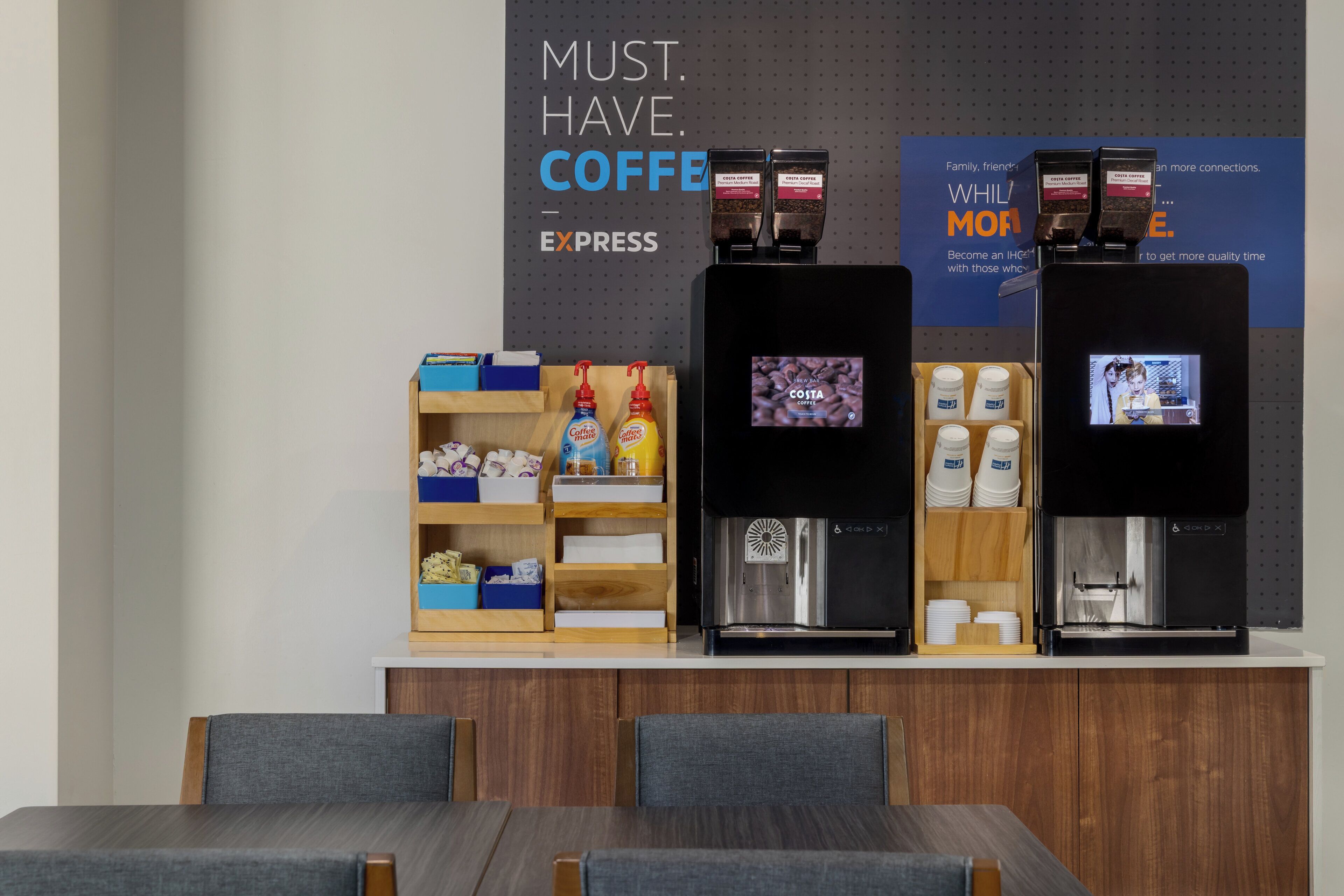 A coffee station with two coffee dispensers, a digital screen, and a shelf with coffee products.