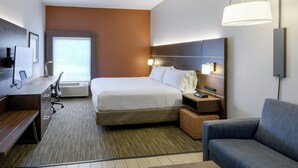 Una habitación de hotel con cama, escritorio, silla, sofá, televisión y lámpara.