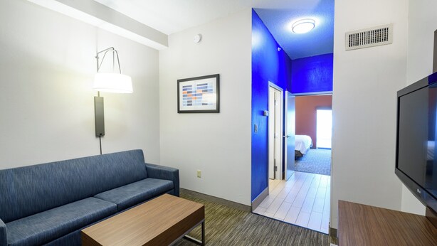Una habitación de hotel moderna con un sofá azul, una mesa de centro de madera, un televisor de pantalla plana y un cuadro en la pared.