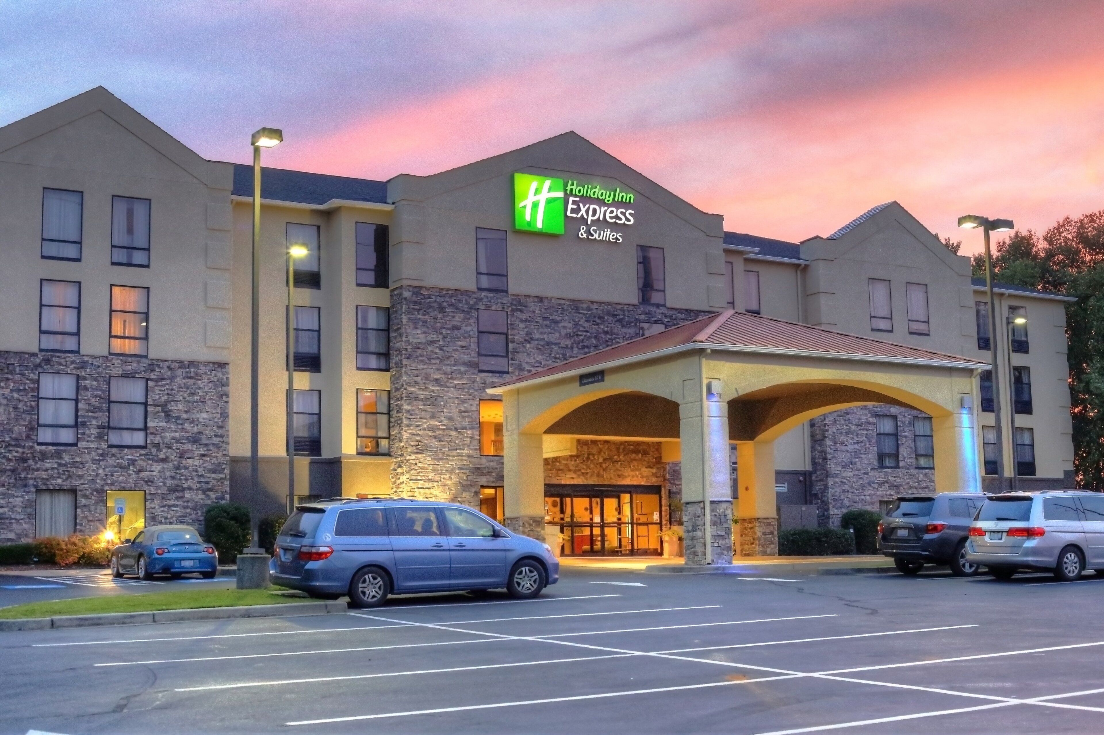 A Holiday Inn Express & Suites building with a stone facade, multiple windows, and a parking lot with several cars.