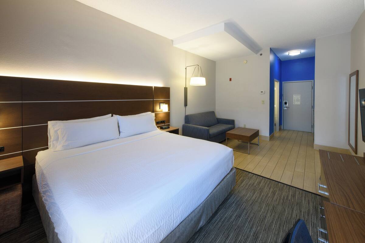 A hotel room with a large bed, bedside tables, a desk, a chair, and a bathroom visible through an open door.