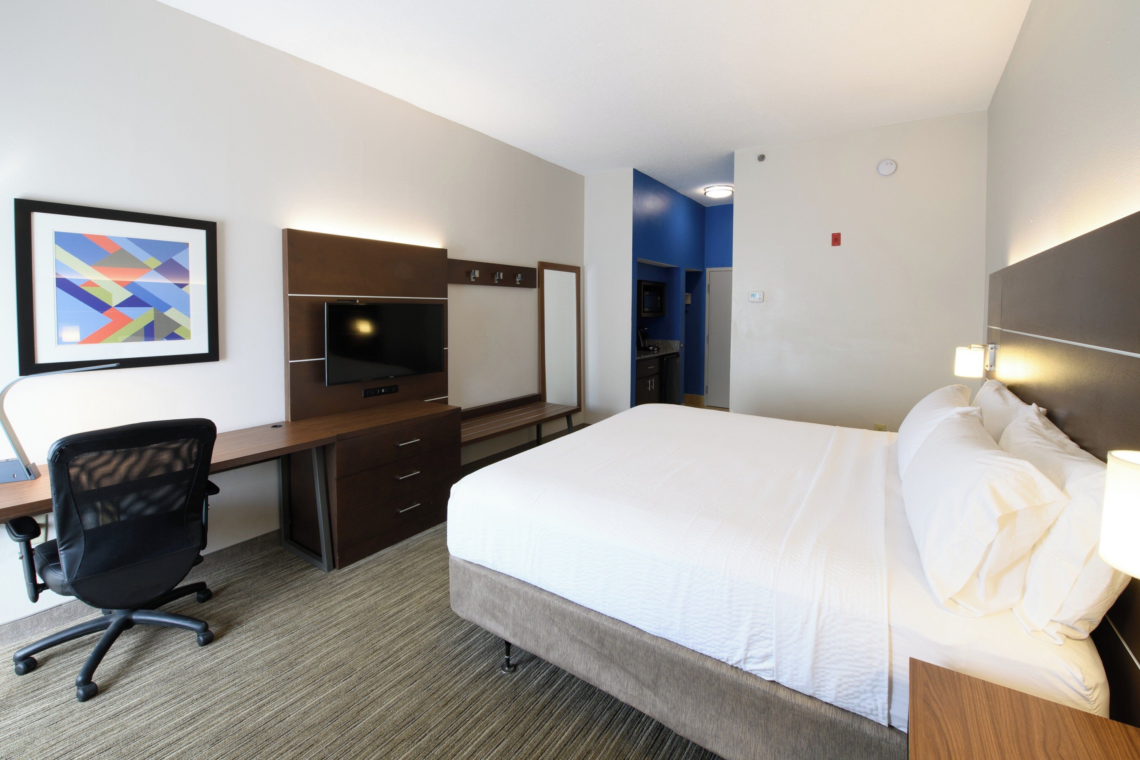 A hotel room with a bed, desk, chair, TV, and a bathroom visible through an open door.