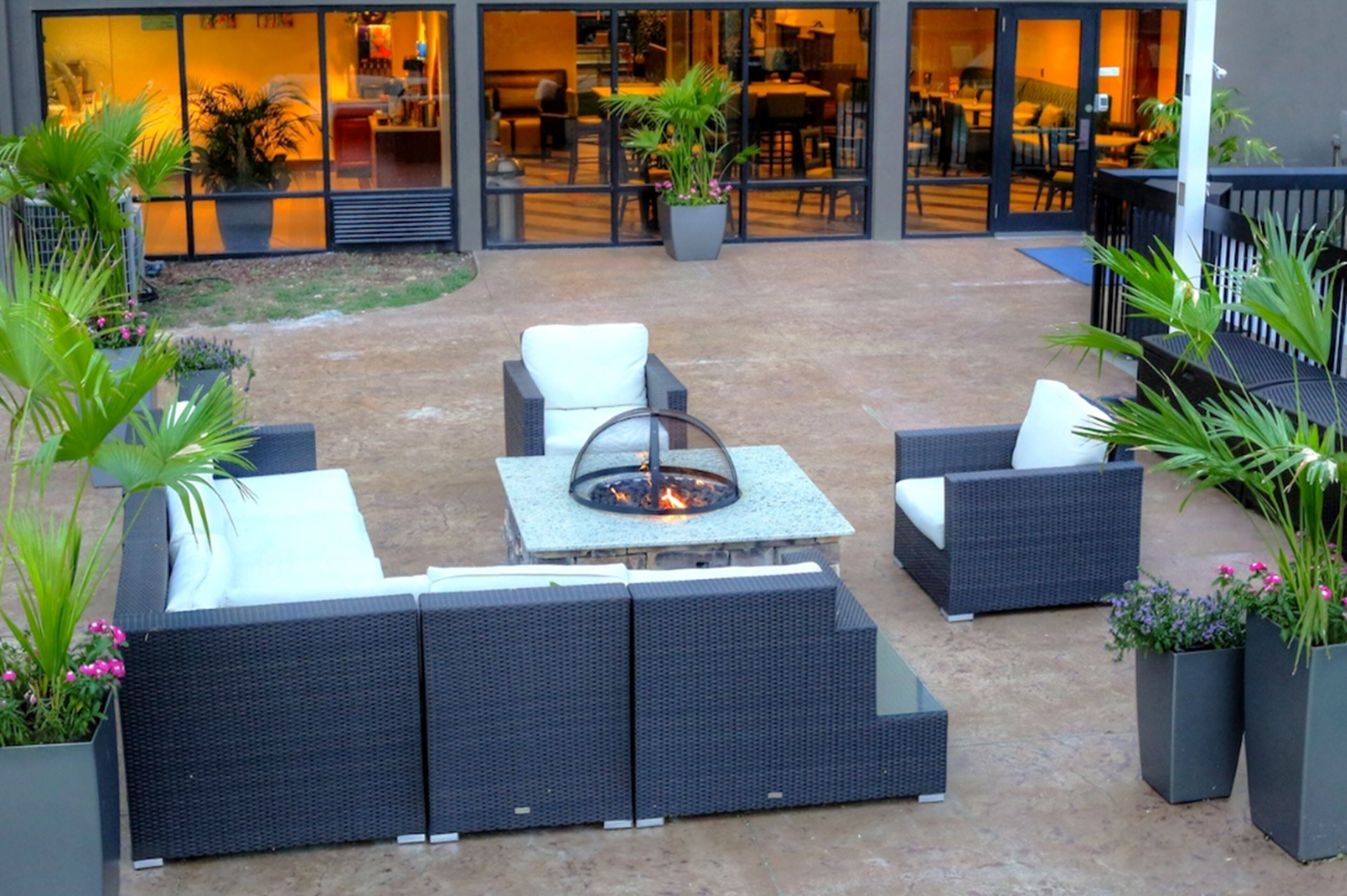 Un espacio al aire libre con una fogata, muebles de mimbre y plantas en macetas.