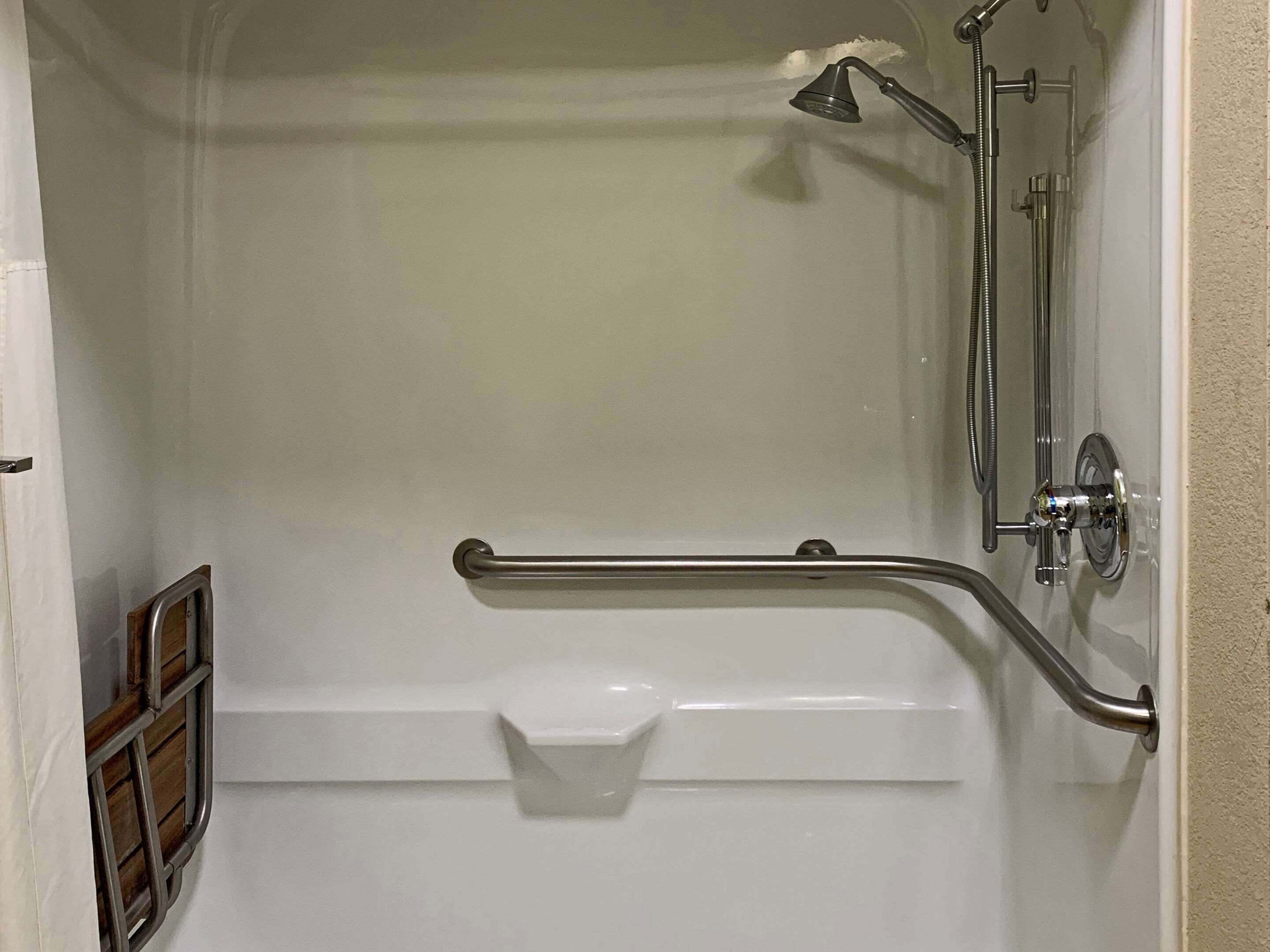 A bathroom with a shower, grab bar, and a white toilet.