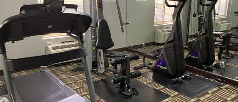 A gym with various exercise equipment, including treadmills and weight machines, and a patterned carpet.
