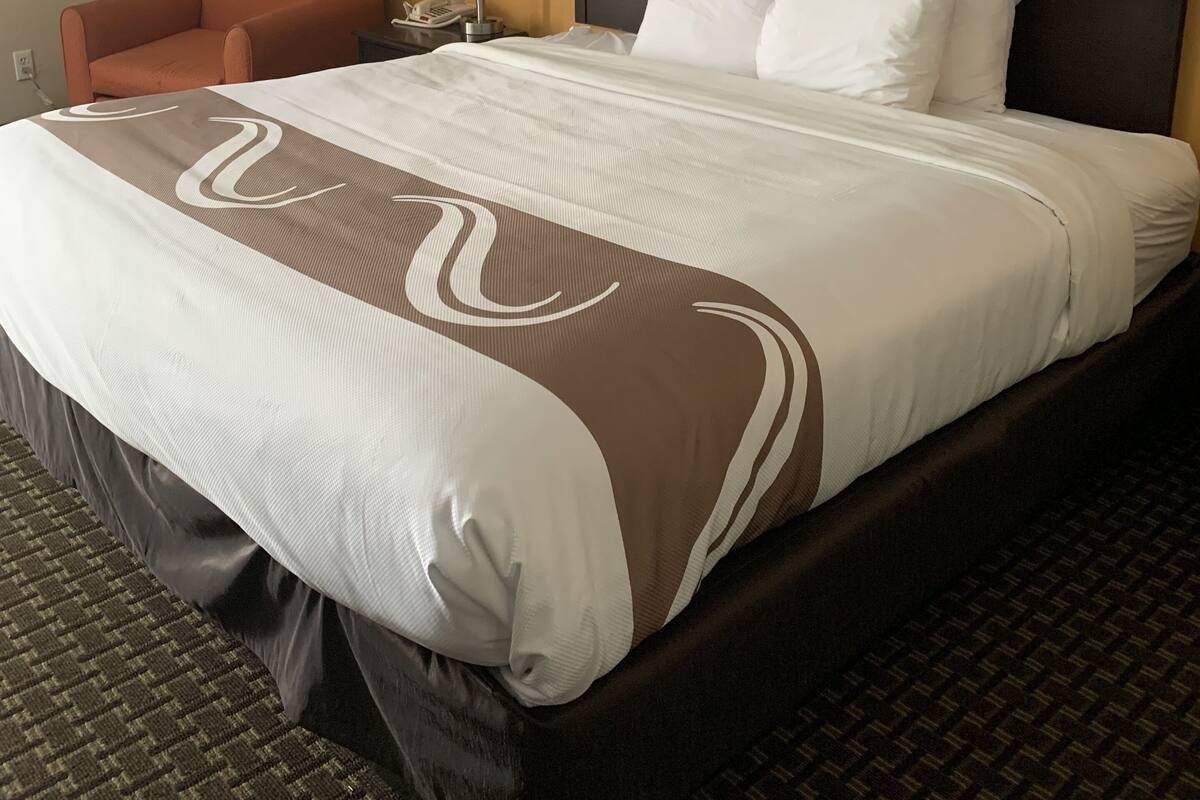 A hotel room with a large bed, a nightstand with a lamp, and a chair.
