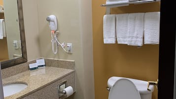 Un baño con encimera de granito, inodoro blanco, toallero con toallas dobladas, secador de pelo y espejo.