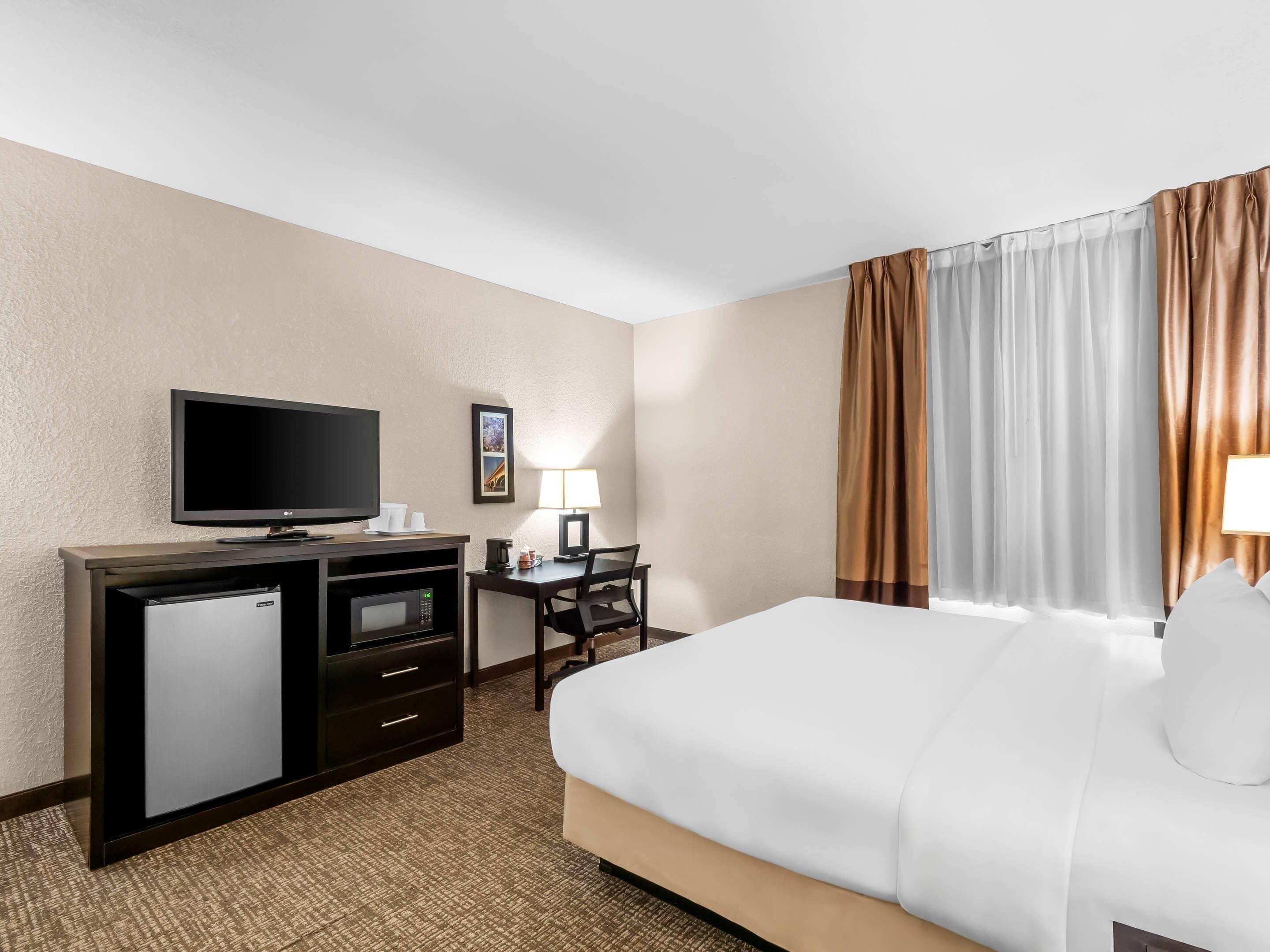 A hotel room with a bed, a TV, a desk with a lamp, and a coffee maker.