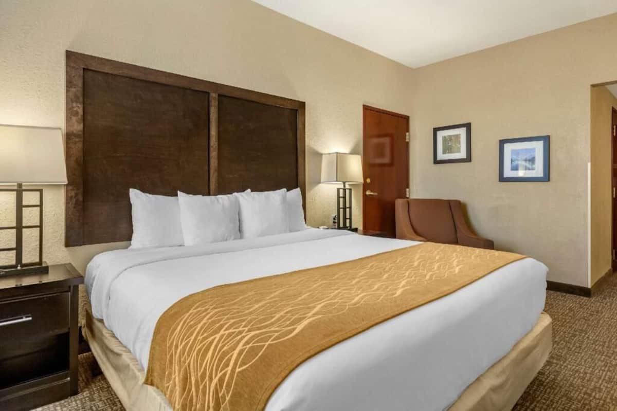 A hotel room with a large bed, a desk, a chair, and a door.