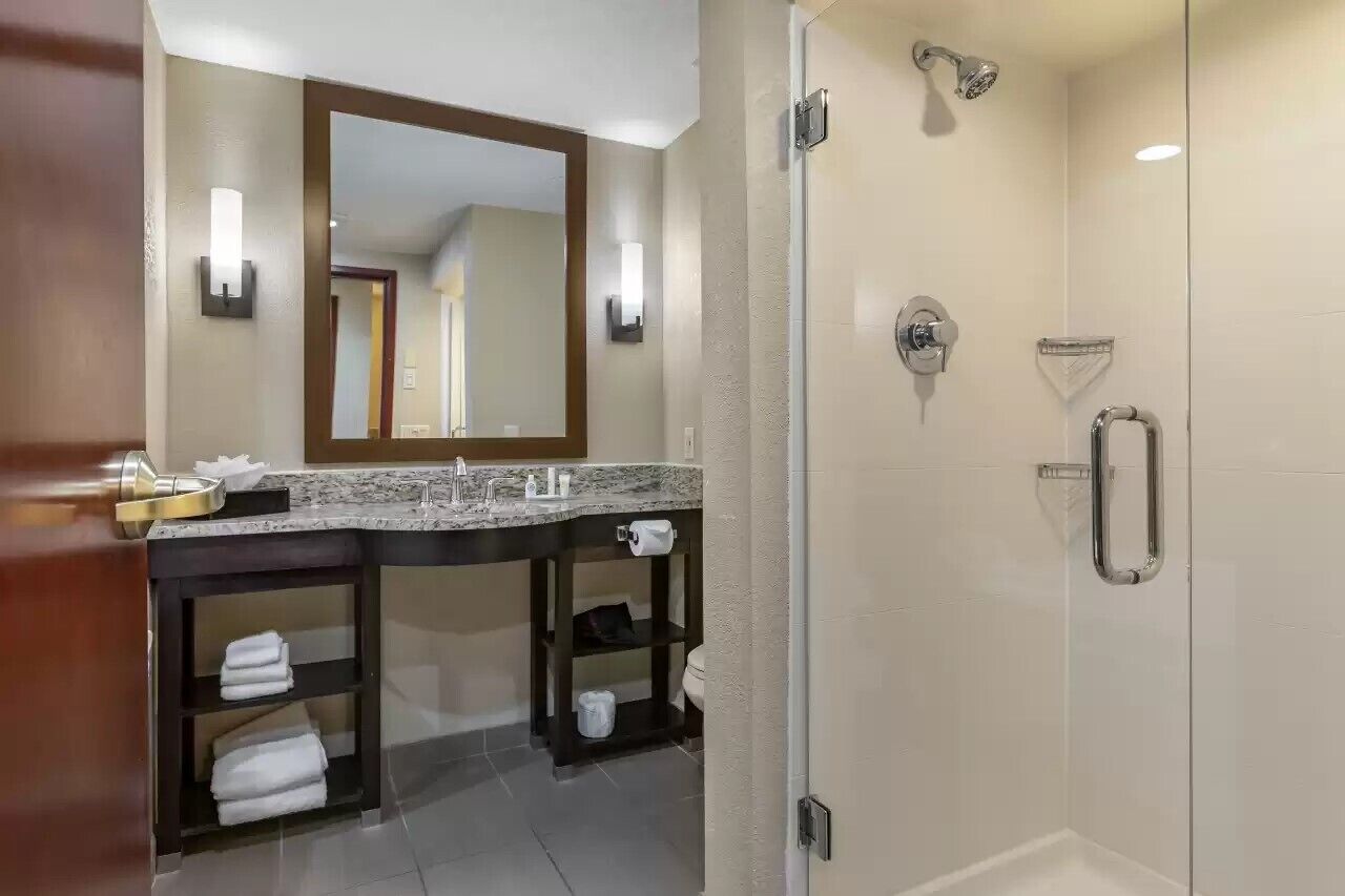 Un baño moderno con un espejo grande, una ducha con cabezal de ducha manual y un lavabo con toalleros.