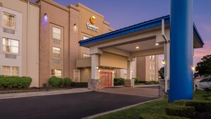 A Comfort Inn & Suites hotel entrance with a covered walkway, stone pillars, and a red door. - Comfort Inn & Suites (Allen Park)