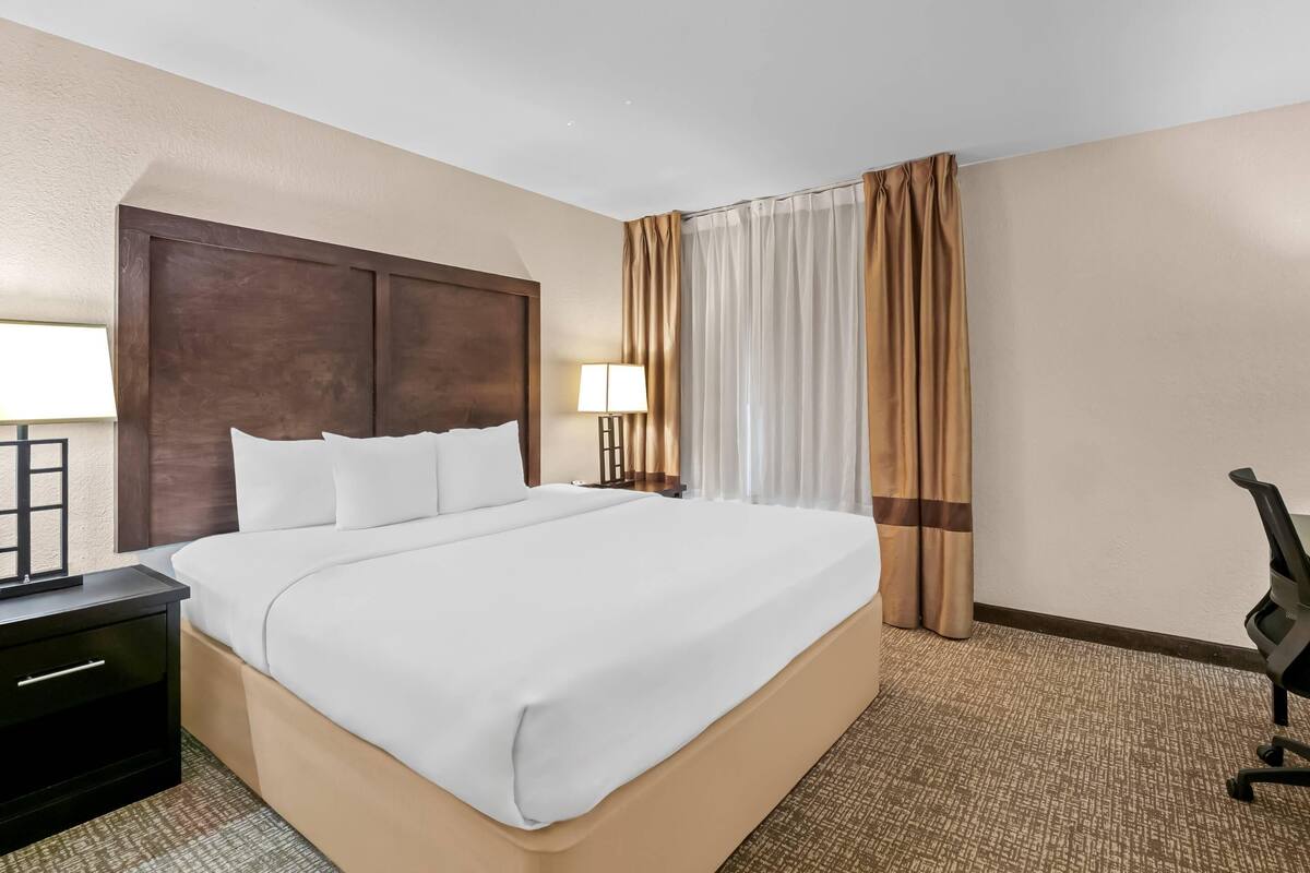 A hotel room with a large bed, two bedside tables, a desk, a chair, and a window with curtains.